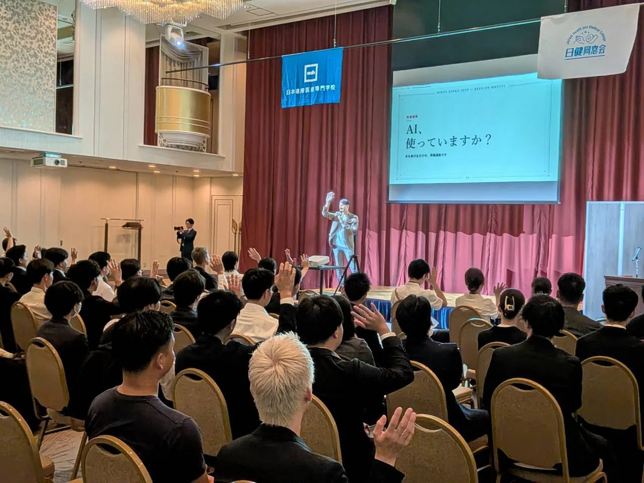 講演会場で手を挙げて参加する皆さん