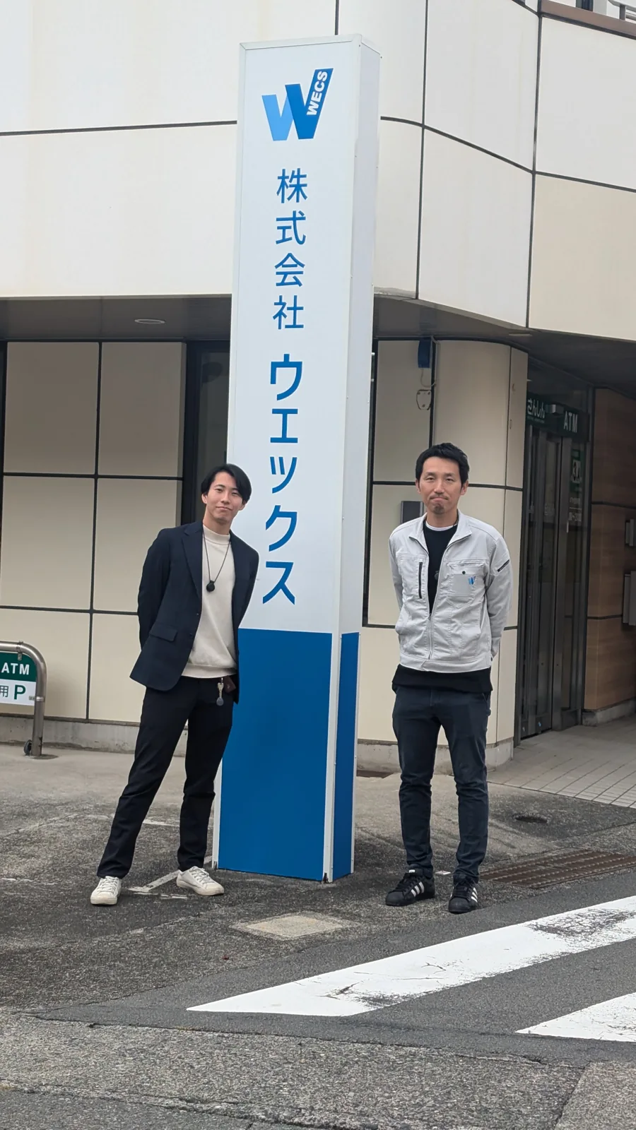 訪問先の看板前で撮影した2名の写真