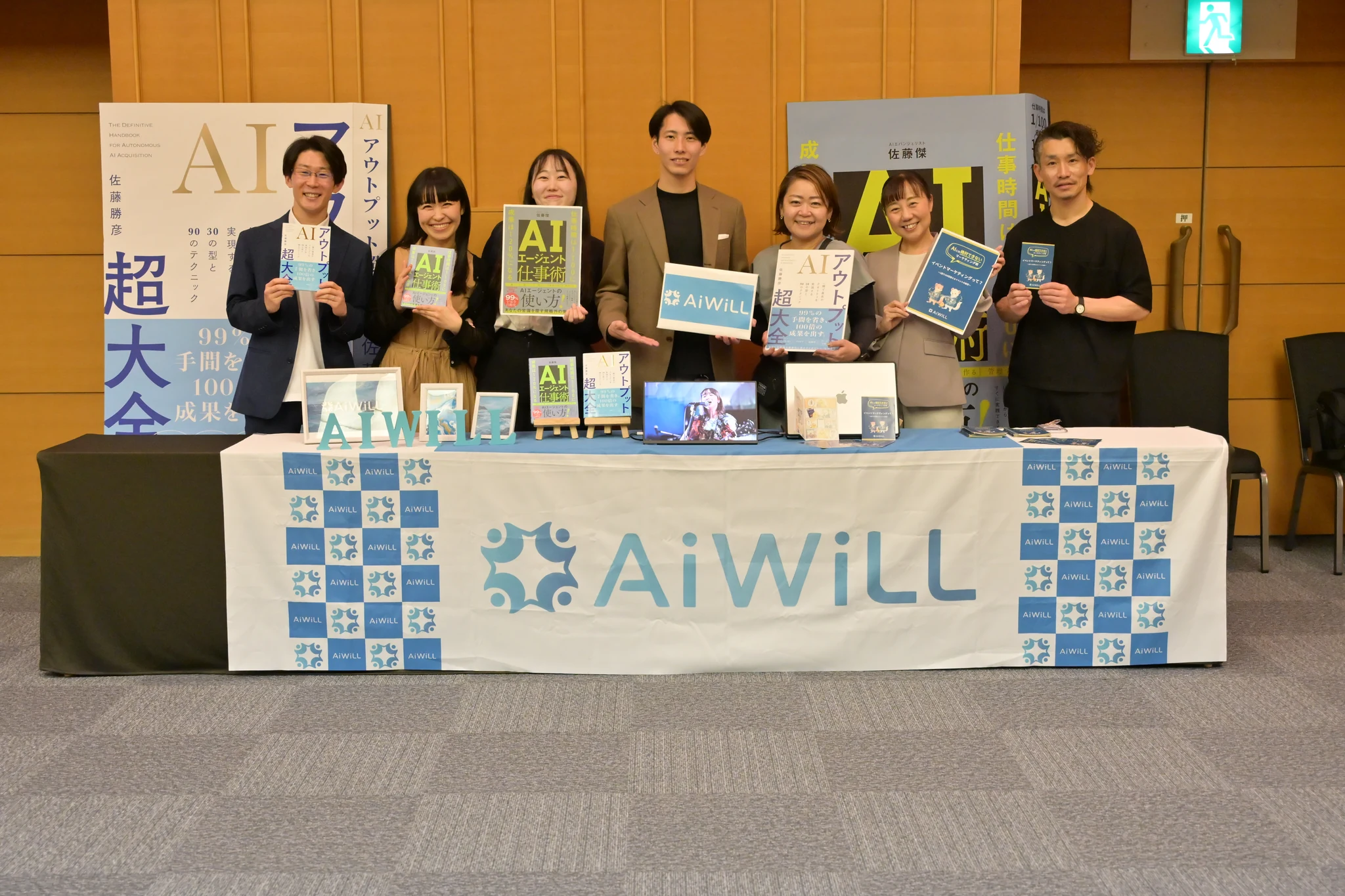 AiWiLLのメンバーが自社の本を手に並んでいる集合写真